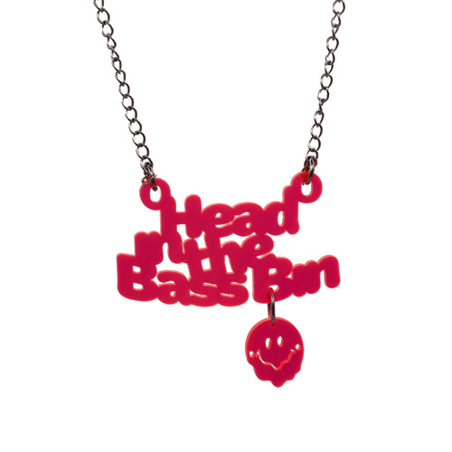 A red acrylic pendant necklace spelling out 'Head in the Bass Bin' with a small matching red smiley face charm hanging below, suspended from a silver-tone chain against a plain white background.