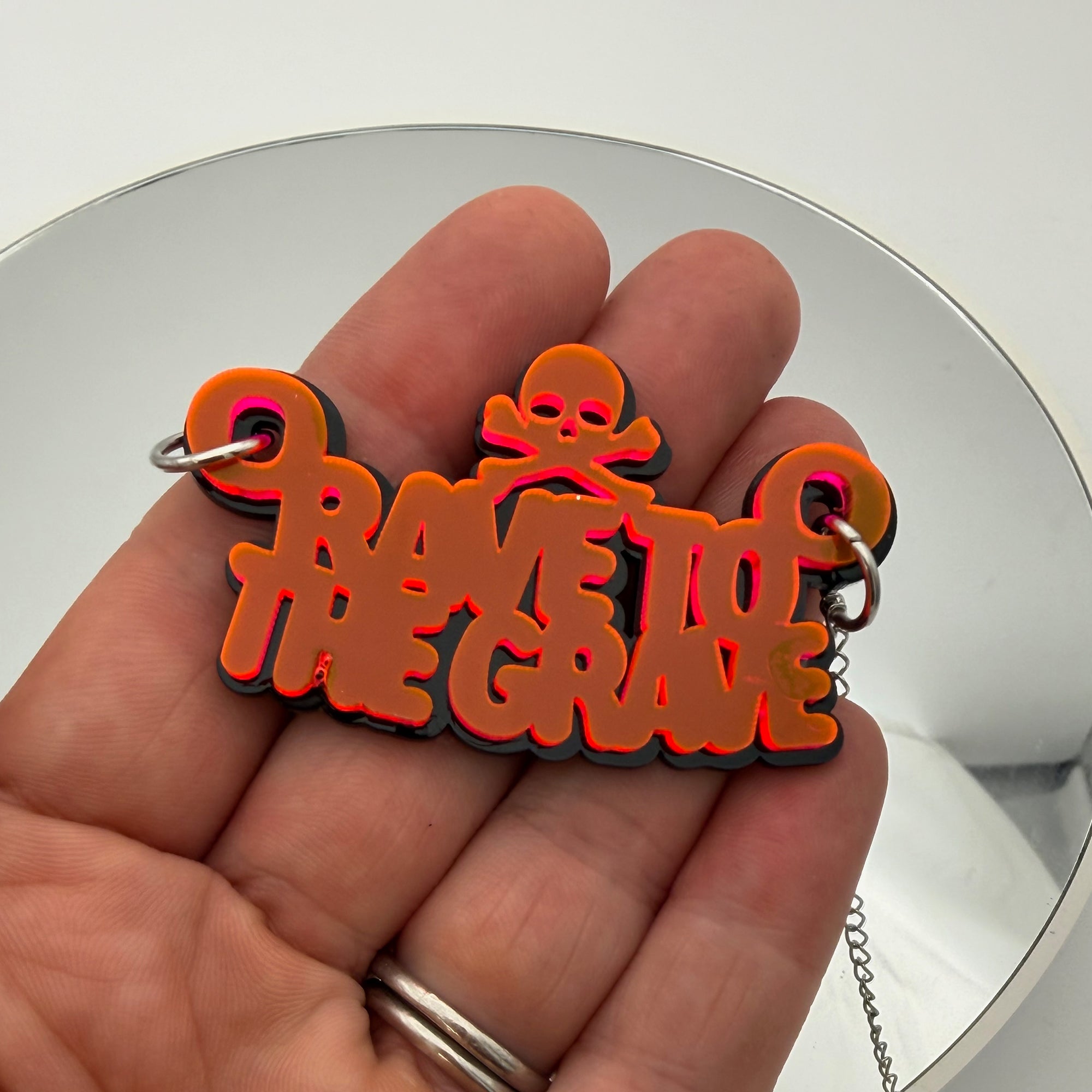 Rave To The Grave Neon Orange and Black Acrylic Necklace on fingertips and mirror background