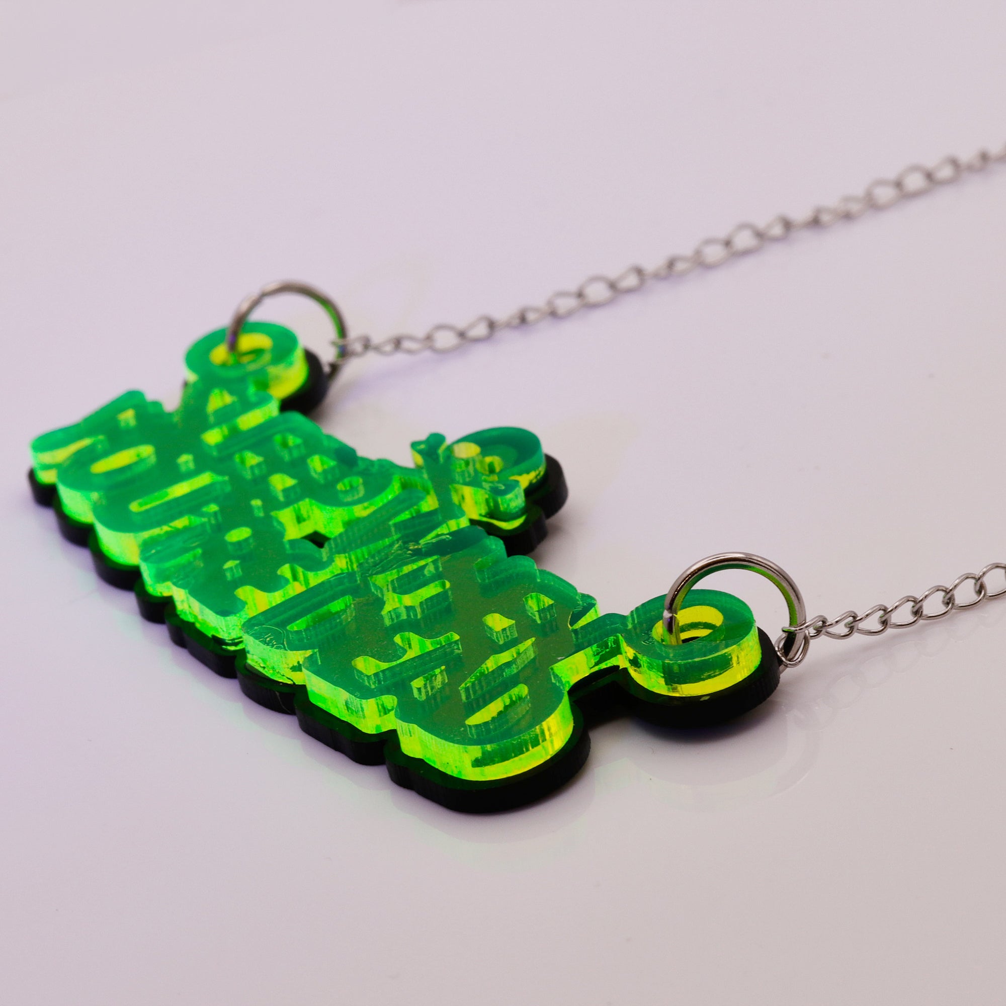 A neon green and black acrylic pendant necklace spelling 'sleep when you're dead' in stylized 3D lettering, suspended from a silver chain on a plain light background.